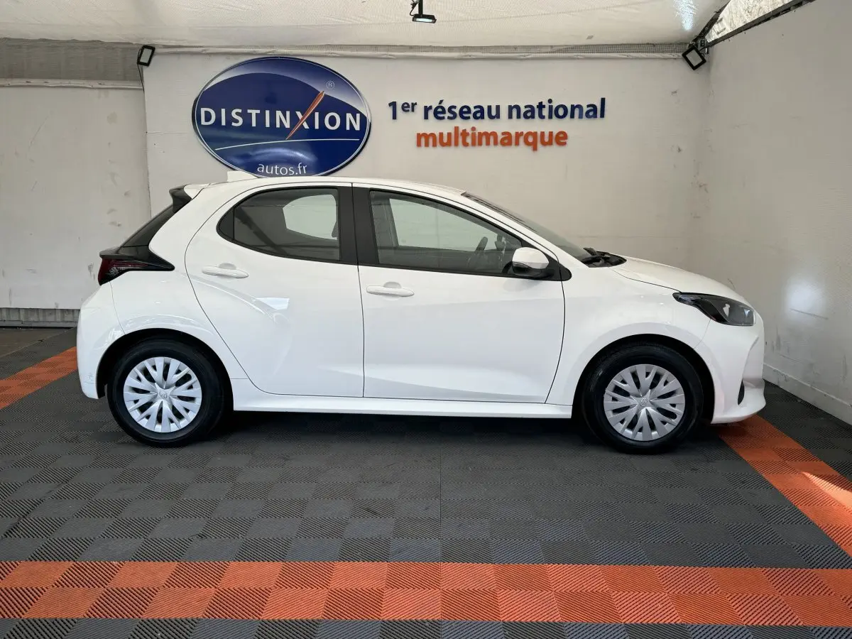 Toyota Yaris hybride blanche vue de profil côté gauche dans un showroom avec logo Distinxion en arrière-plan.