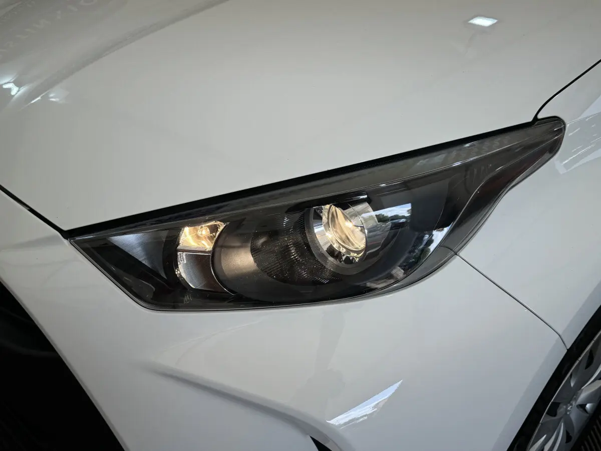 Gros plan sur le phare avant droit de la Toyota Yaris hybride blanche, soulignant son design moderne et épuré.