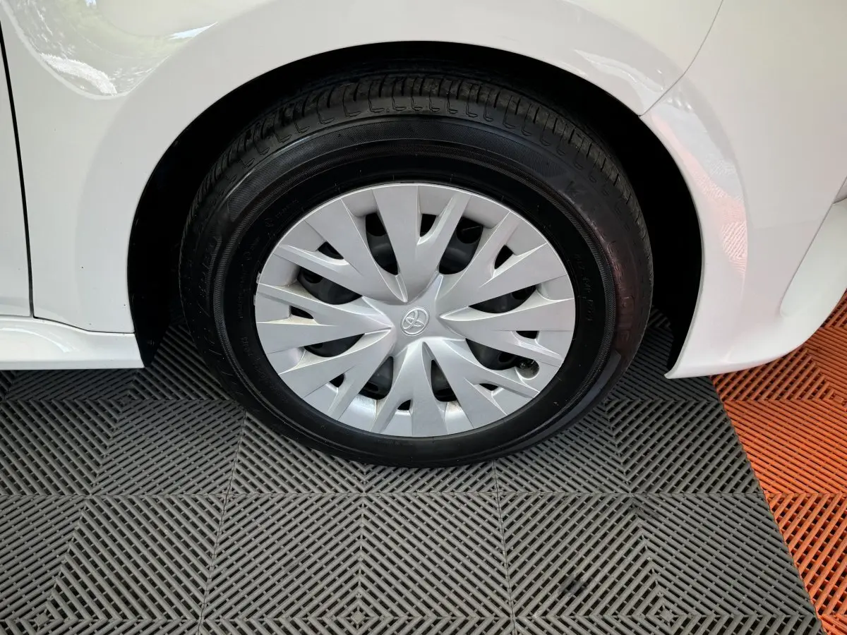 Gros plan sur la roue avant droite d'une Toyota Yaris hybride blanche, avec enjoliveur argenté au design moderne.