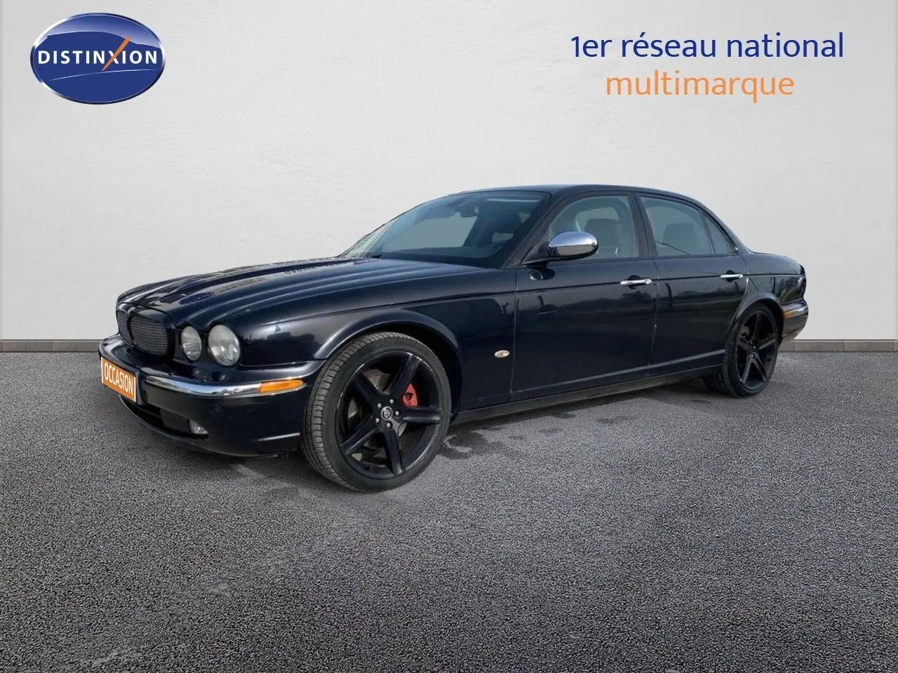 Jaguar XJ6 noir en 3/4 avant droit, avec jantes noires à cinq branches et étriers de frein rouges visibles.