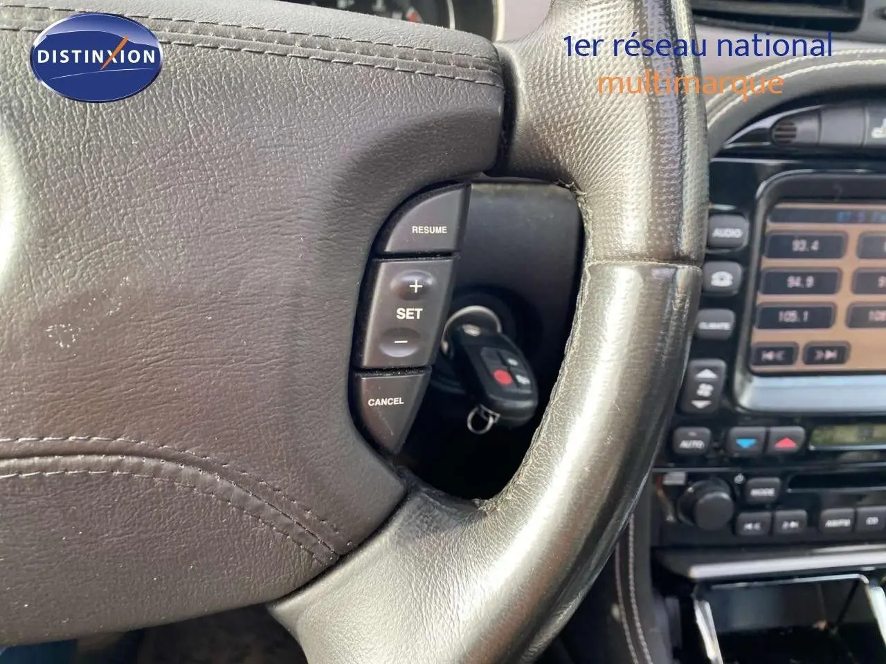 Gros plan sur le volant en cuir noir de la Jaguar XJ6 2.7 V6 Biturbo, avec commandes de régulateur de vitesse visibles.