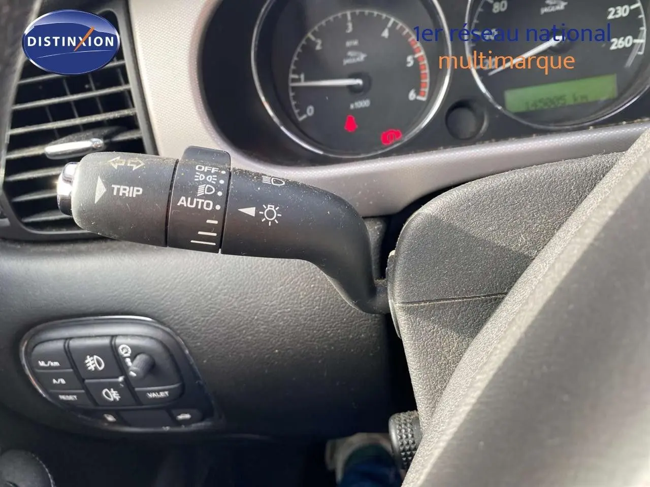 Gros plan sur la manette de clignotant et tableau de bord de la Jaguar XJ6 noire, affichant le compteur et commandes.
