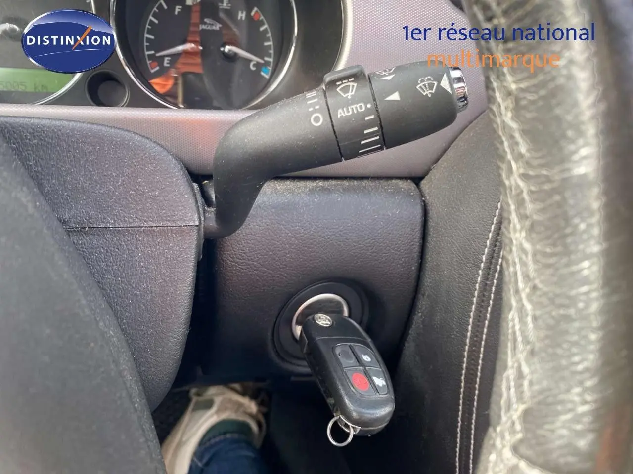 Gros plan intérieur sur le contacteur avec clé Jaguar insérée, volant cuir noir visible en partie à droite.