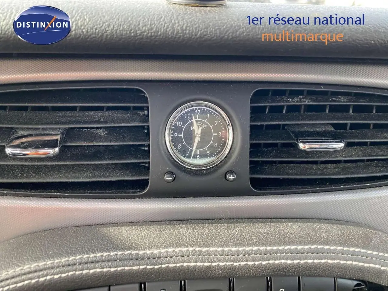 Gros plan sur l'horloge centrale et les aérateurs du tableau de bord de la Jaguar XJ6 noire de 2006.