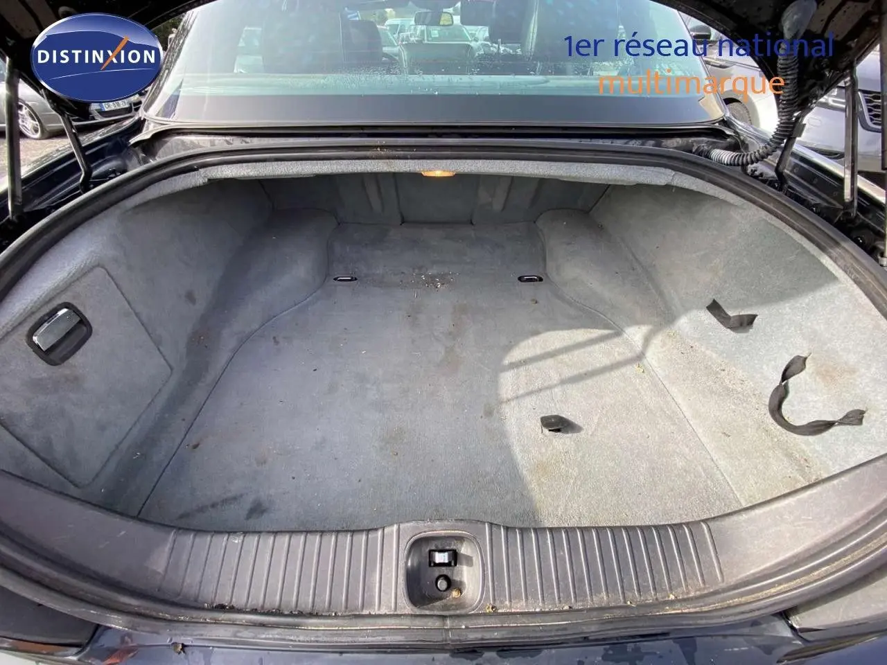 Coffre ouvert vu de l'arrière d'une Jaguar XJ6 noire de 2006, montrant un espace de rangement vide et tapissé.