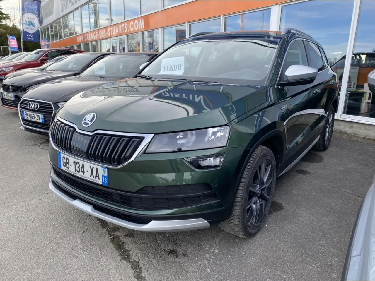 Skoda Karoq Scout vert foncé vu en 3/4 avant droit, avec jantes noires et coques de rétroviseurs blanches.