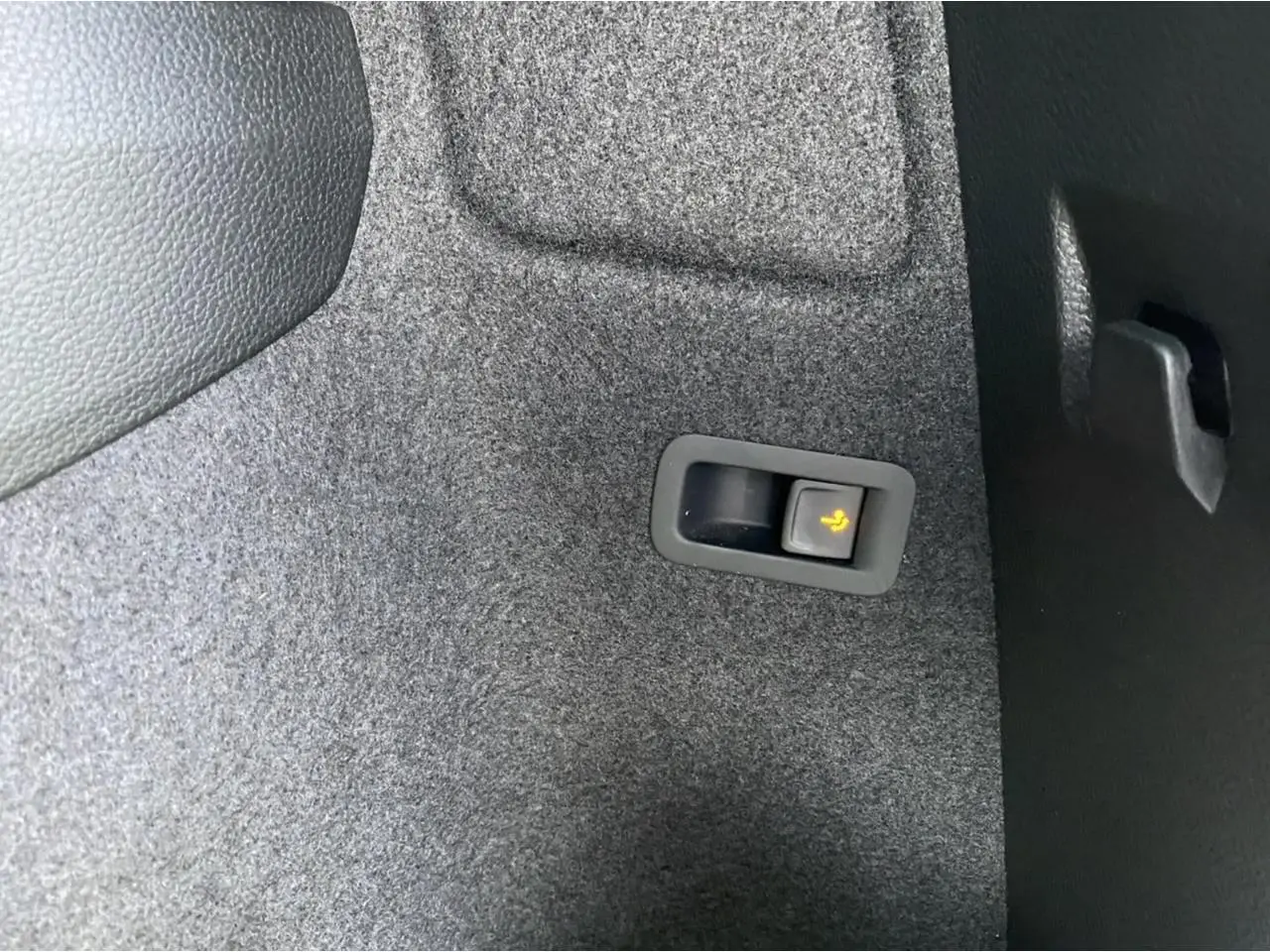 Détail du bouton de rabattement électrique des sièges dans le coffre du Skoda Karoq Scout vert foncé, vue intérieure.