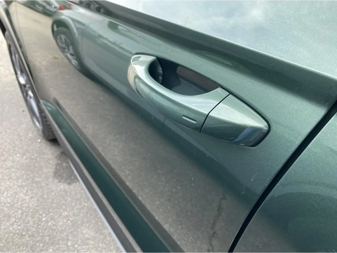 Gros plan sur la poignée de porte côté gauche d’un Skoda Karoq Scout vert foncé 2021, reflet sur la carrosserie.