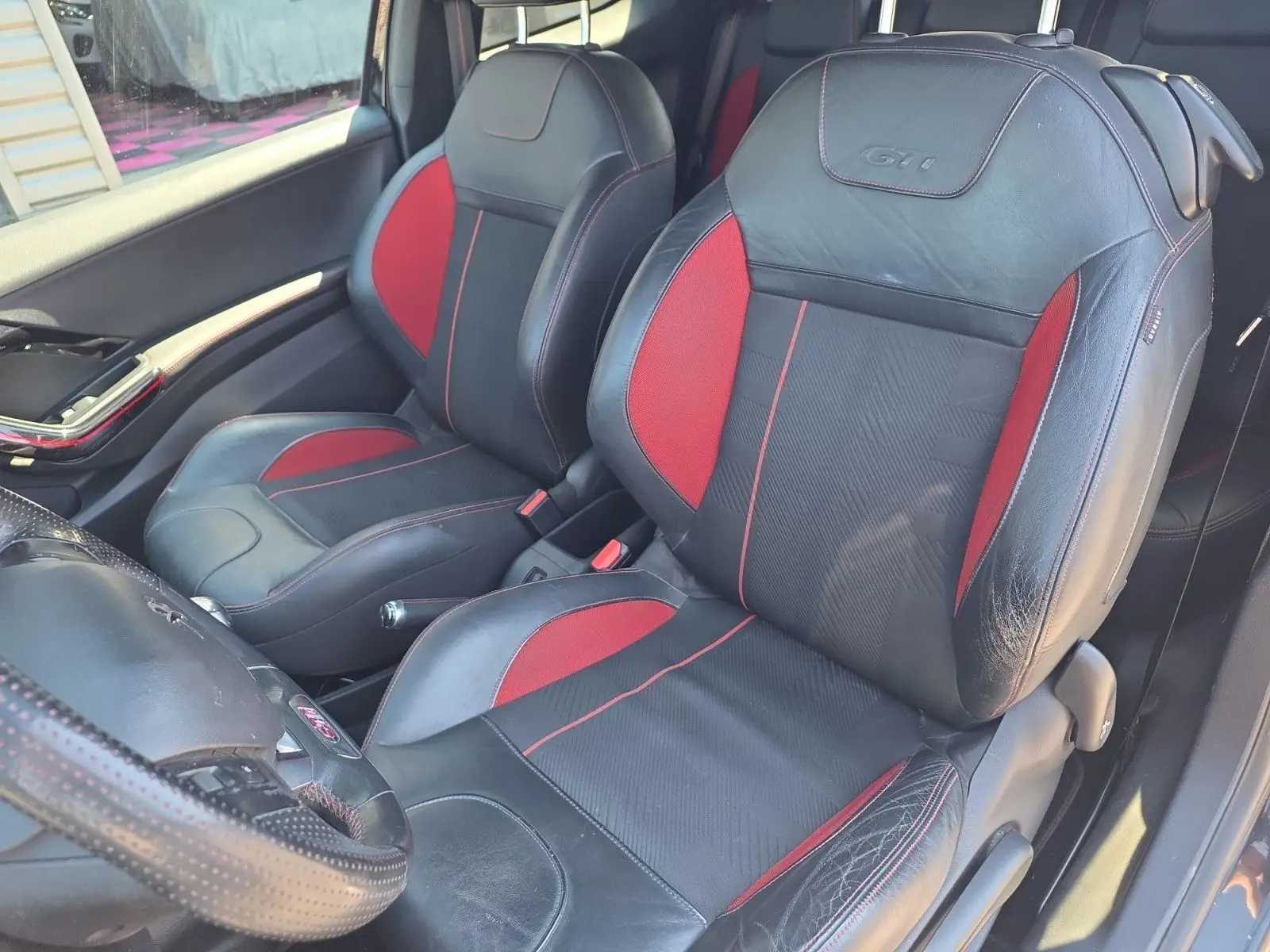 Vue intérieure côté gauche montrant les sièges baquets cuir et alcantara noirs et rouges avec logo GTI sur Peugeot 208 GTI.