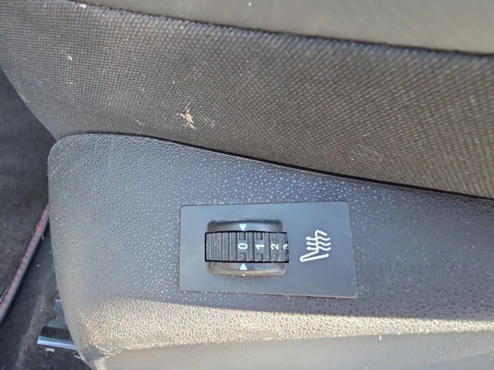 Gros plan sur le bouton de réglage des sièges chauffants noirs dans une Peugeot 208 GTI 2015.