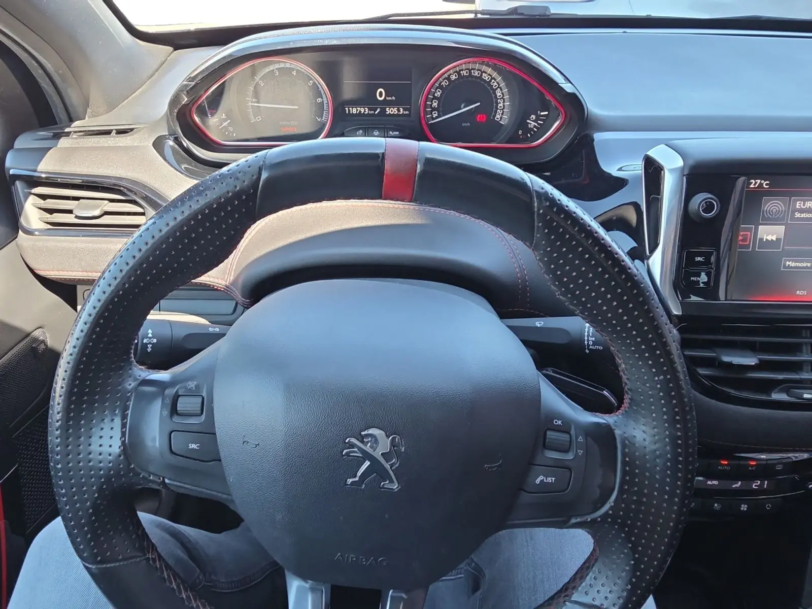 Vue intérieure centrée sur le volant sport en cuir perforé avec bande rouge de la Peugeot 208 GTI noire de 2015.