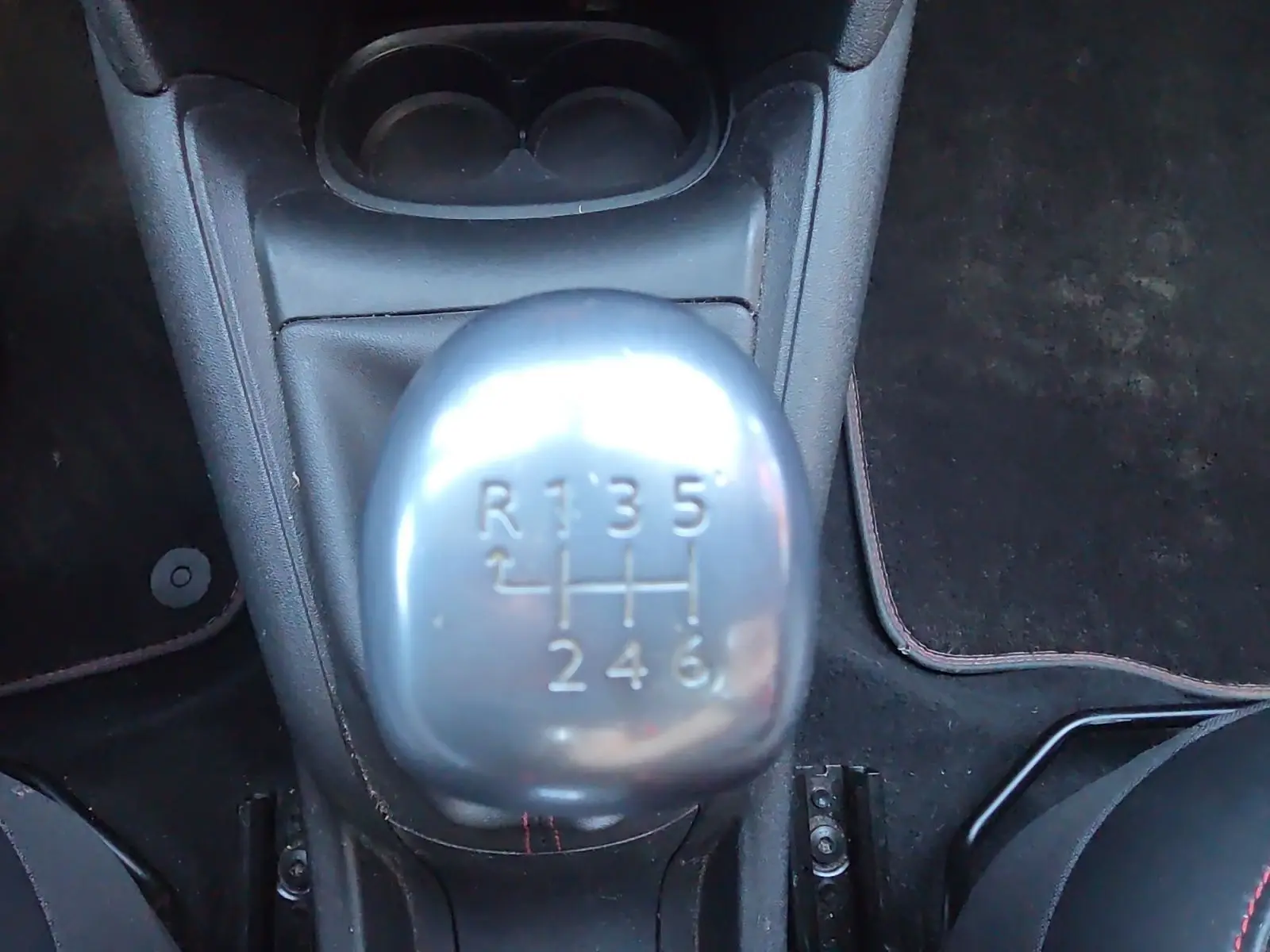 Gros plan sur le levier de vitesses manuel argenté de la Peugeot 208 GTI noire, entouré de tapis noirs et sièges sport.