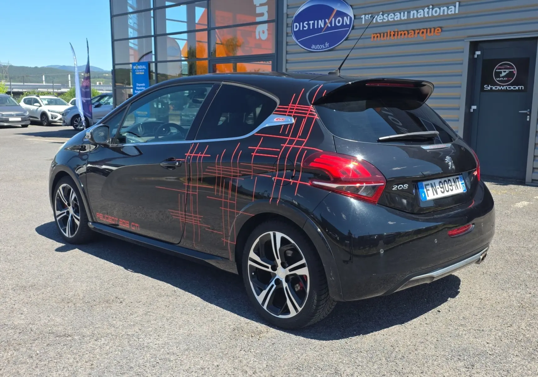 Peugeot 208 GTI noire vue 3/4 arrière droit avec jantes alliage 17” et décorations rouges sportives sur la carrosserie.