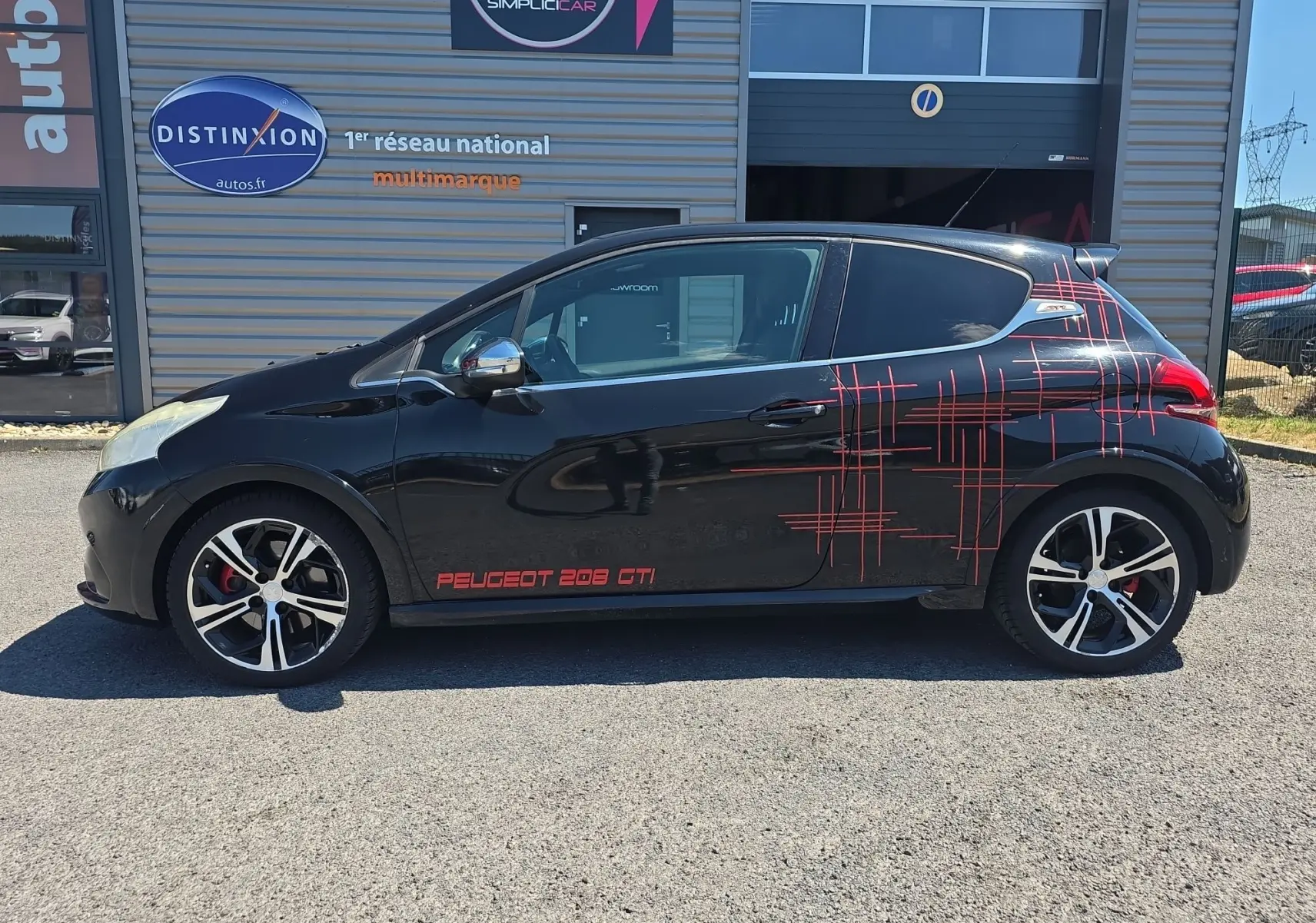 Profil côté gauche d'une Peugeot 208 GTI noire de 2015 avec jantes alliage 17” et décor rouge graphique sur la carrosserie.