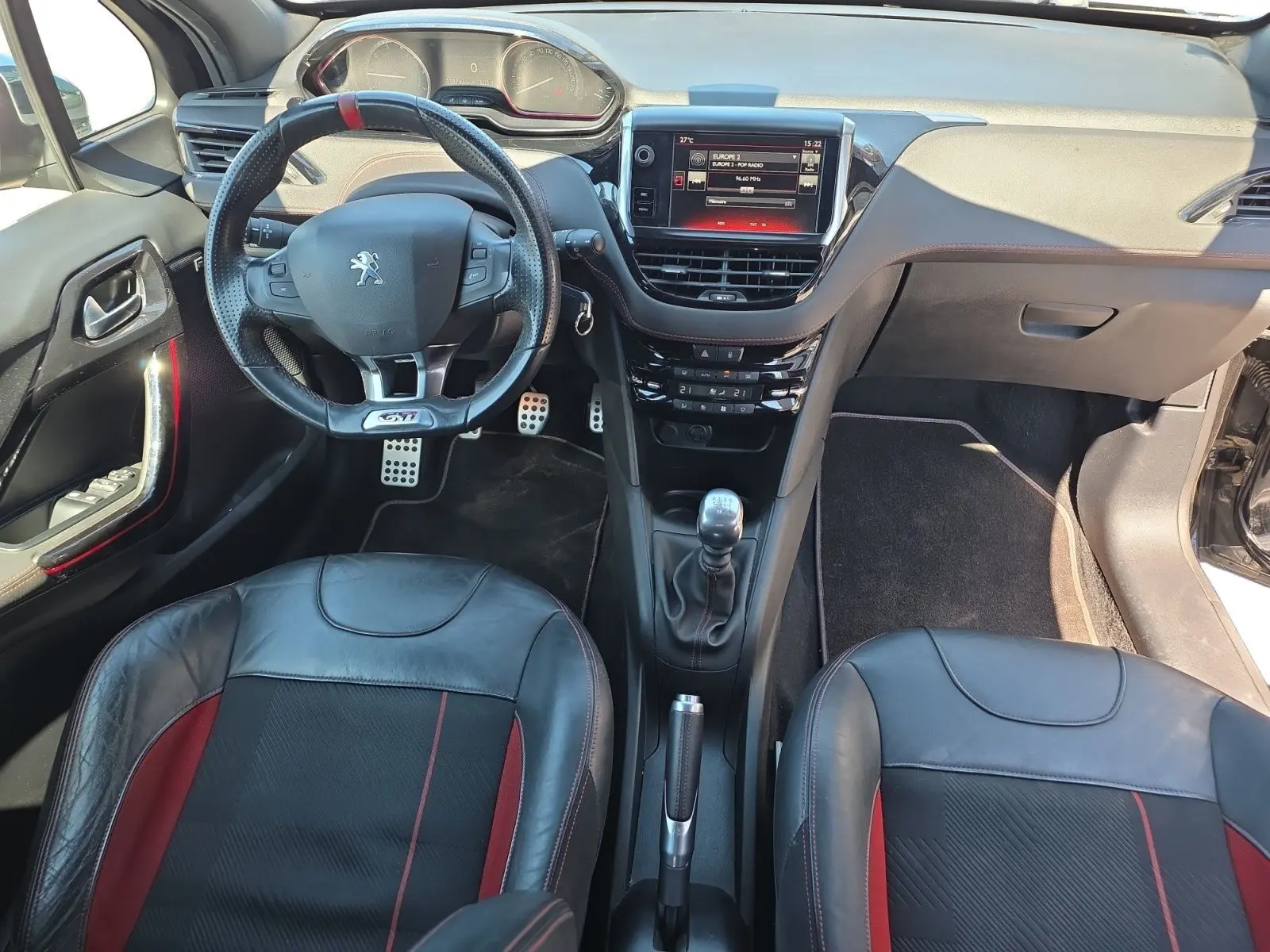 Vue intérieure frontale de la Peugeot 208 GTI 2015 noire, avec volant sport GTI, sellerie cuir/alcantara et écran tactile central.