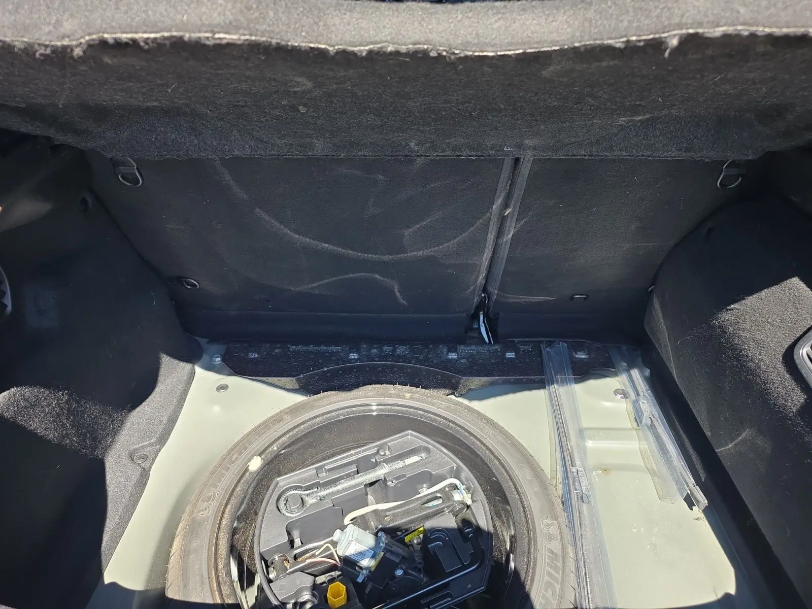 Coffre ouvert vu de dessus d'une Peugeot 208 GTI noire, montrant la roue de secours et les outils de bord.