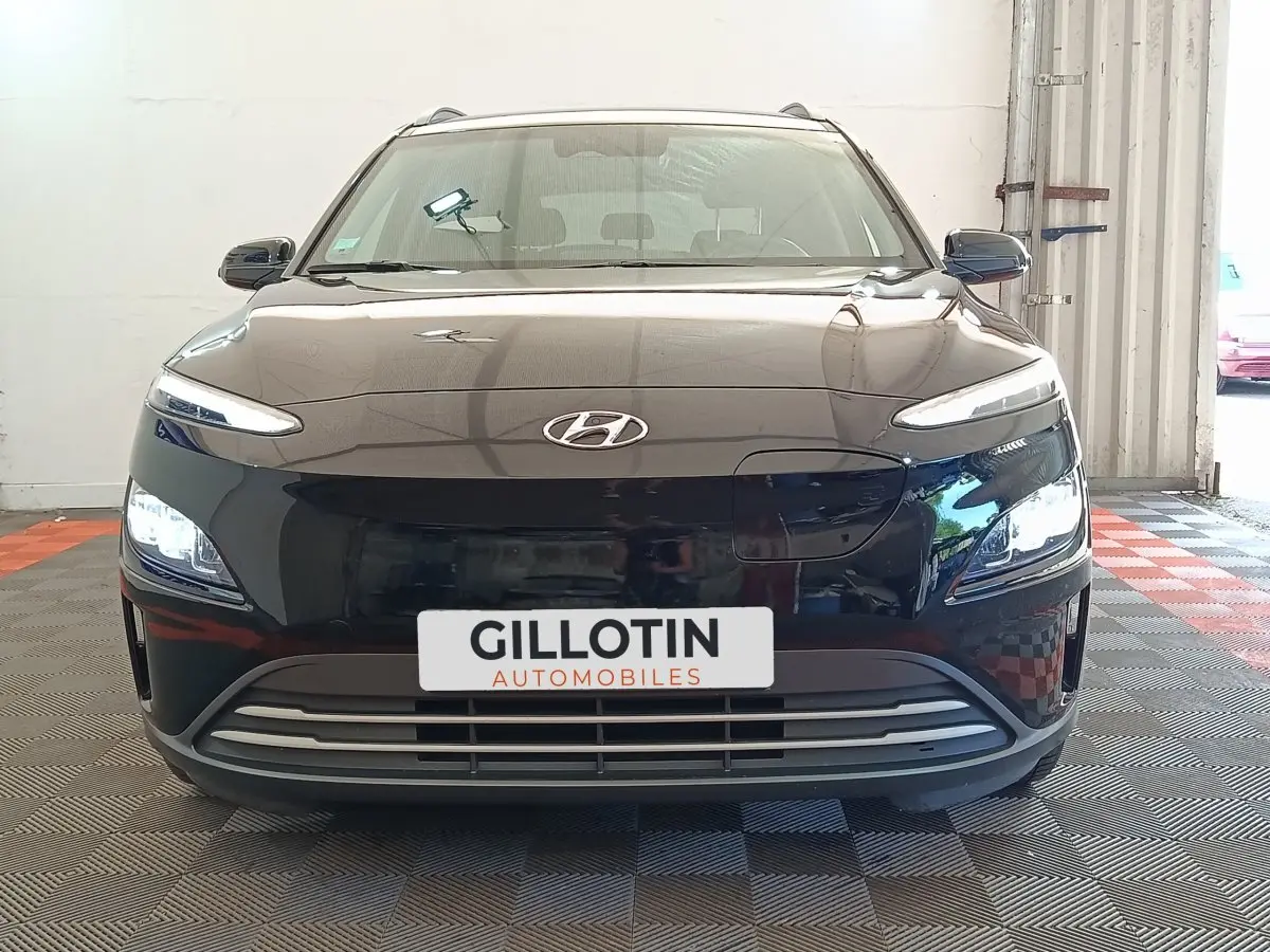 Vue de face d'un Hyundai Kona électrique noir 2023 avec phares LED allumés dans un garage.