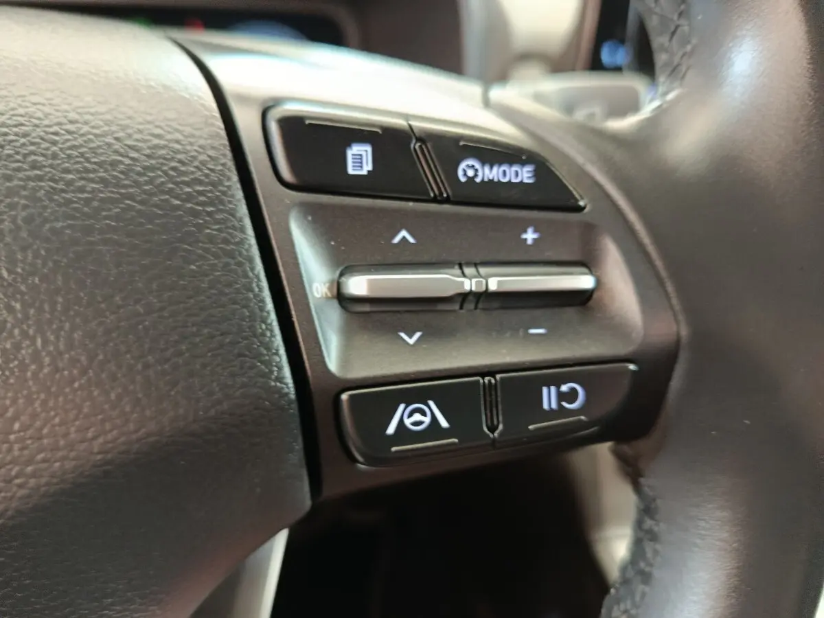 Gros plan sur les commandes du volant cuir noir du Hyundai Kona électrique 2023, boutons de régulateur adaptatif et assistance au maintien de voie.