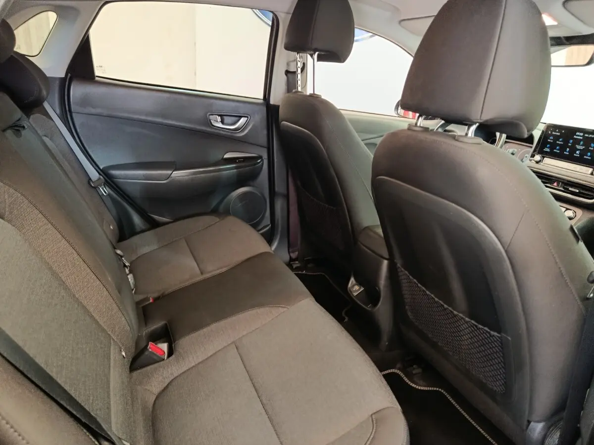Vue intérieure arrière du Hyundai Kona électrique 2023, sièges tissu gris et dossier avant en cuir noir.