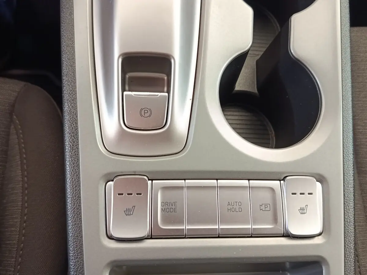 Vue rapprochée de la console centrale argentée du Hyundai Kona électrique 2023, avec boutons de chauffage sièges et frein à main électrique.