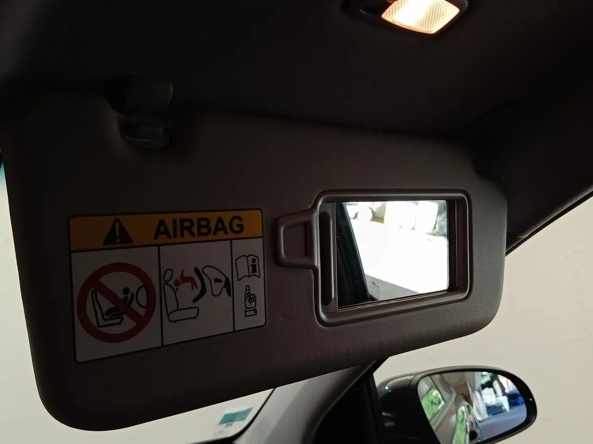 Miroir de pare-soleil côté conducteur avec avertissement airbag, vue intérieure du toit et rétroviseur latéral noir visible.