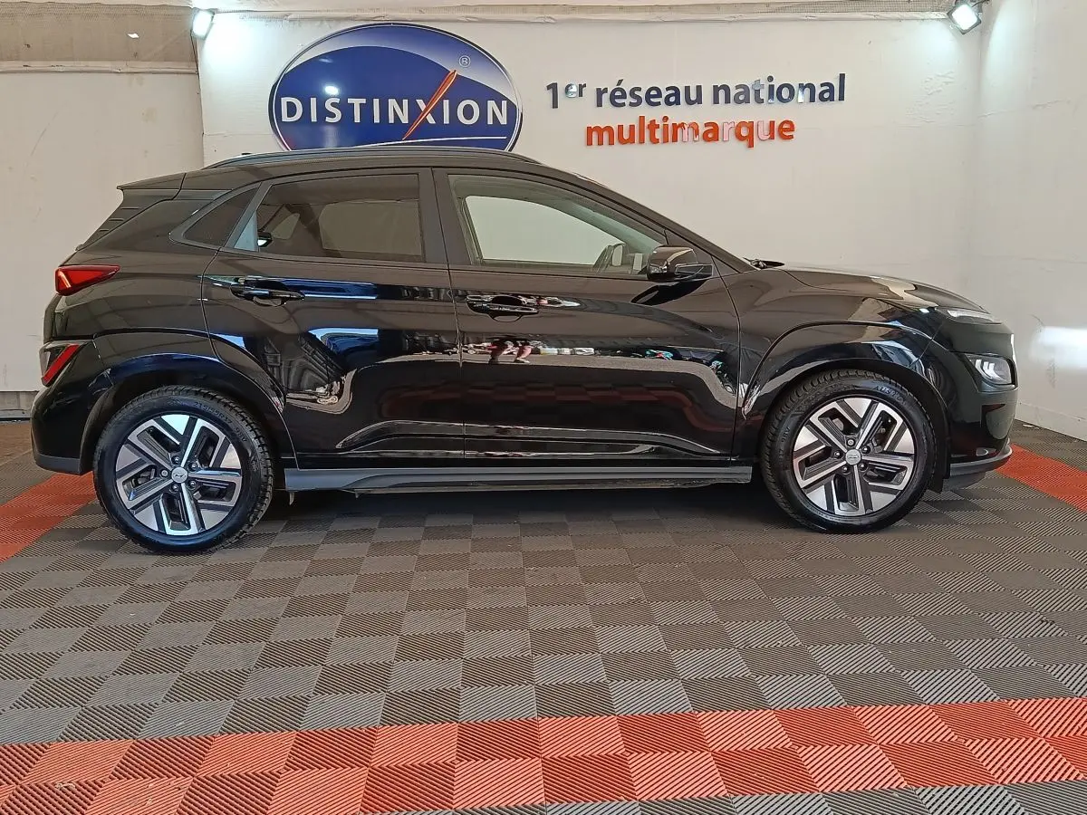 Vue de profil côté gauche d'un Hyundai Kona électrique noir 2023, avec jantes modernes et toit noir mat.
