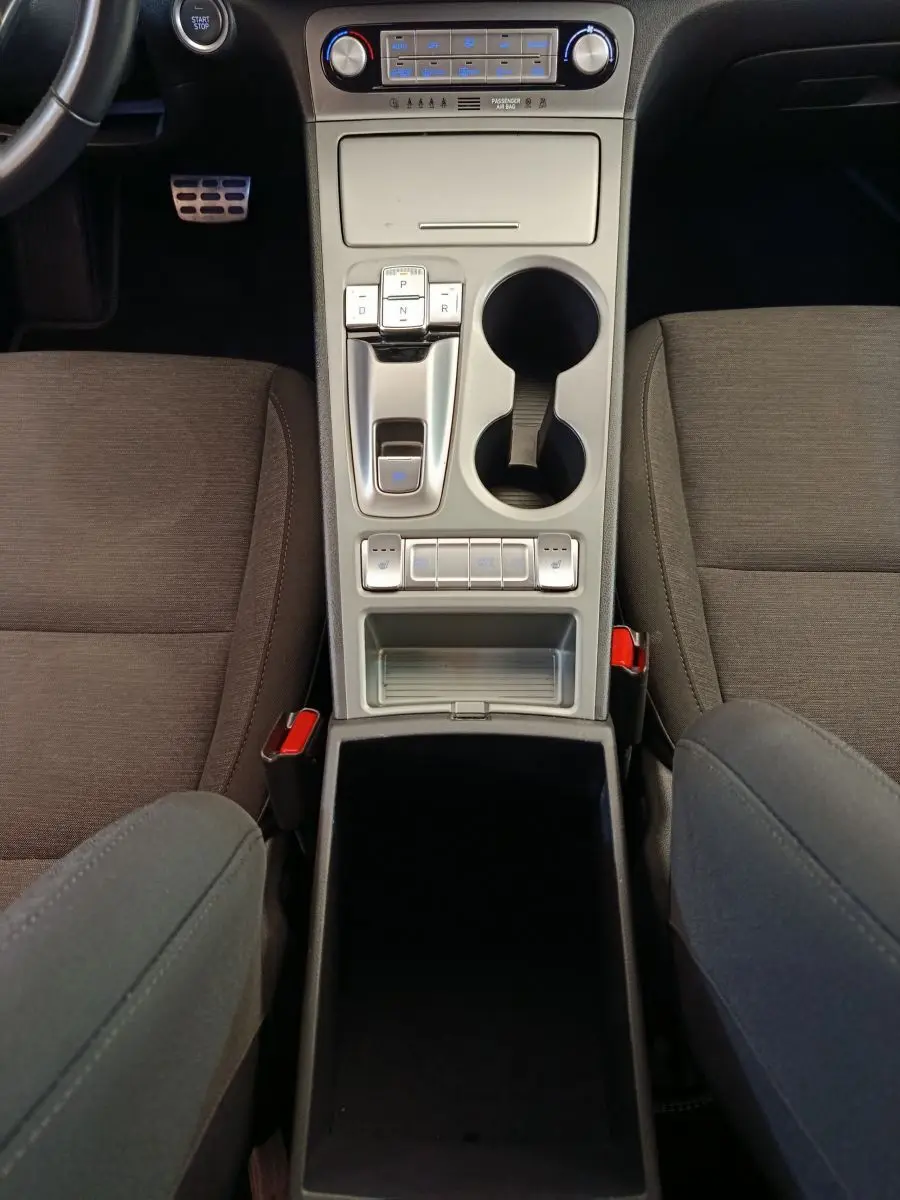 Vue plongeante sur la console centrale grise du Hyundai Kona électrique 2023, avec commandes de boîte auto et porte-gobelets.