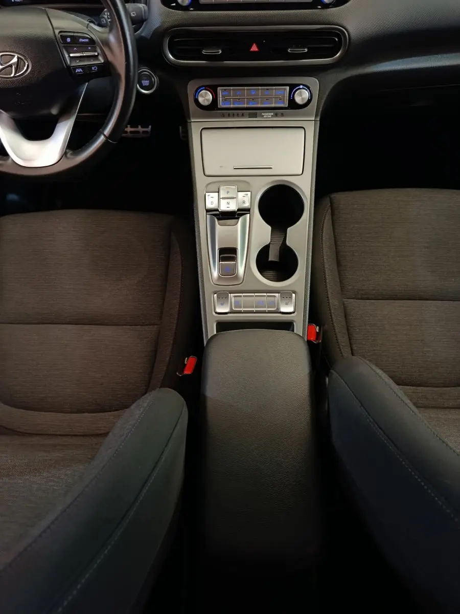Vue intérieure plongeante sur la console centrale grise et les sièges tissu noirs du Hyundai Kona électrique 2023.
