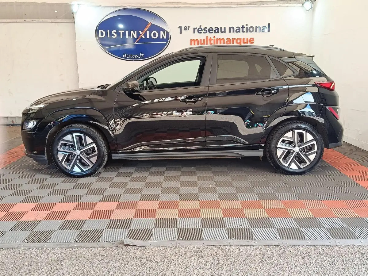 Vue de profil côté gauche d’un Hyundai Kona électrique noir 2023, avec jantes alliage et toit noir contrasté.