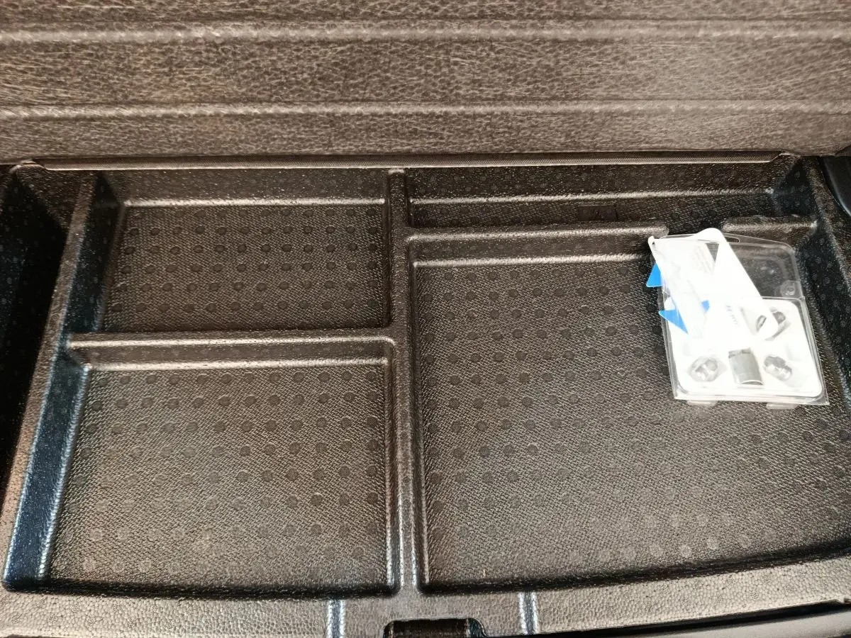 Rangement sous plancher de coffre noir du Hyundai Kona électrique 2023 avec compartiments et accessoires visibles.