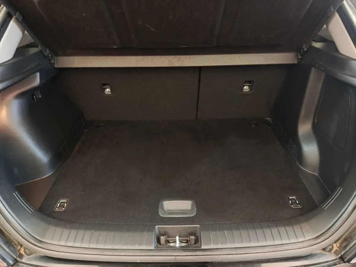 Coffre ouvert vu de l'arrière d'un Hyundai Kona électrique noir, espace de chargement vide et tapis noir.