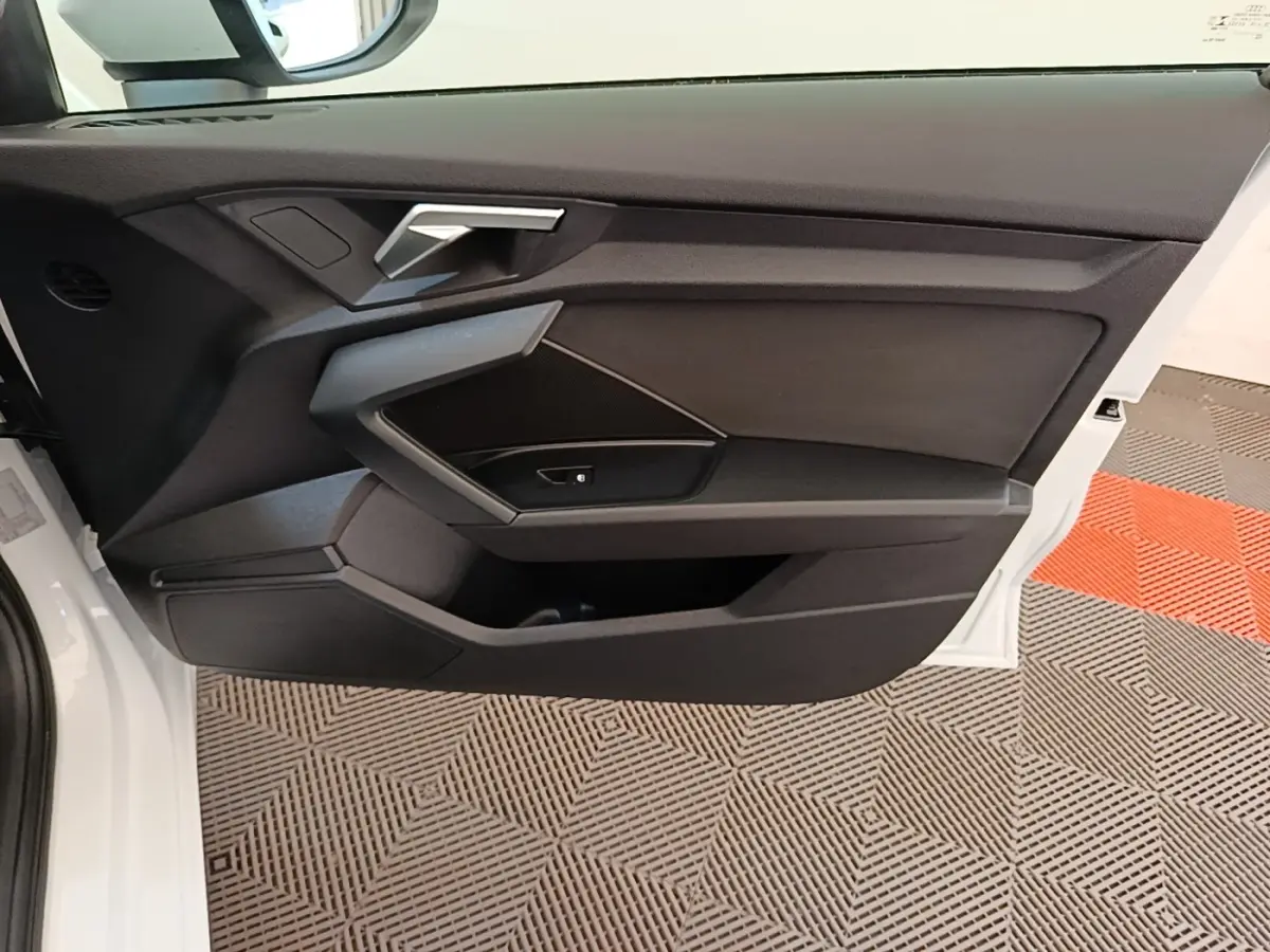 Vue intérieure côté gauche de la porte avant blanche d'une Audi A3 40 TFSI e avec garniture noire et poignée argentée.