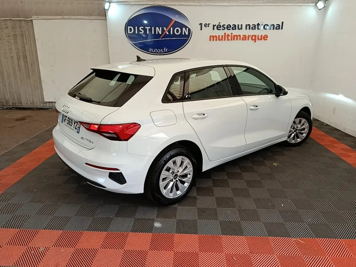 Audi A3 40 TFSI e blanche vue 3/4 arrière droit dans un showroom avec logo Distinxion en arrière-plan.