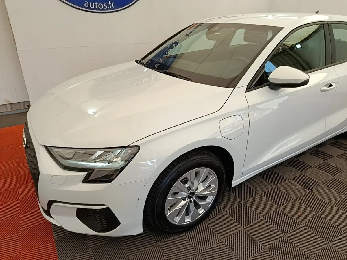 Audi A3 40 TFSI e blanc en 3/4 avant droit, avec prises de recharge et phares LED visibles.