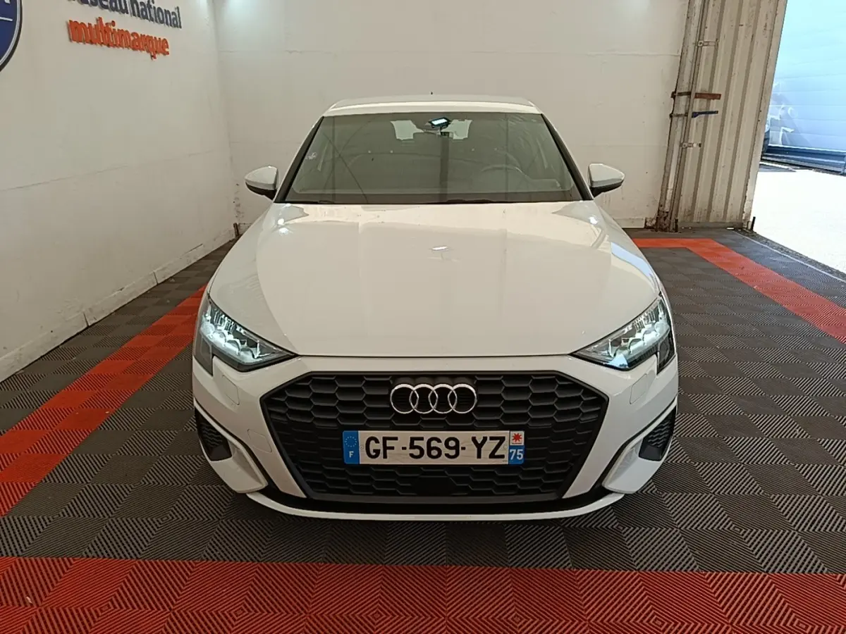 Audi A3 blanc vue de face dans un garage, avec calandre noire et phares LED allumés.