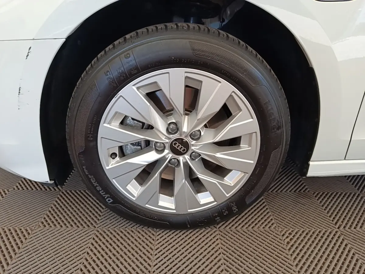 Gros plan sur la roue avant gauche d’une Audi A3 blanche, mettant en valeur la jante en alliage et le logo Audi central.