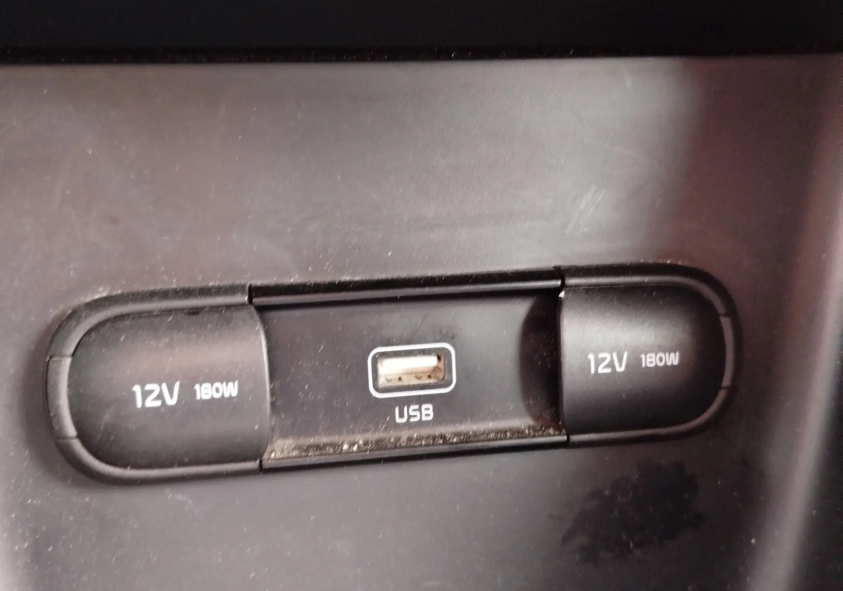 Prise USB et deux prises 12V 180W noires en gros plan dans l'habitacle du Kia Sportage blanc 2022.