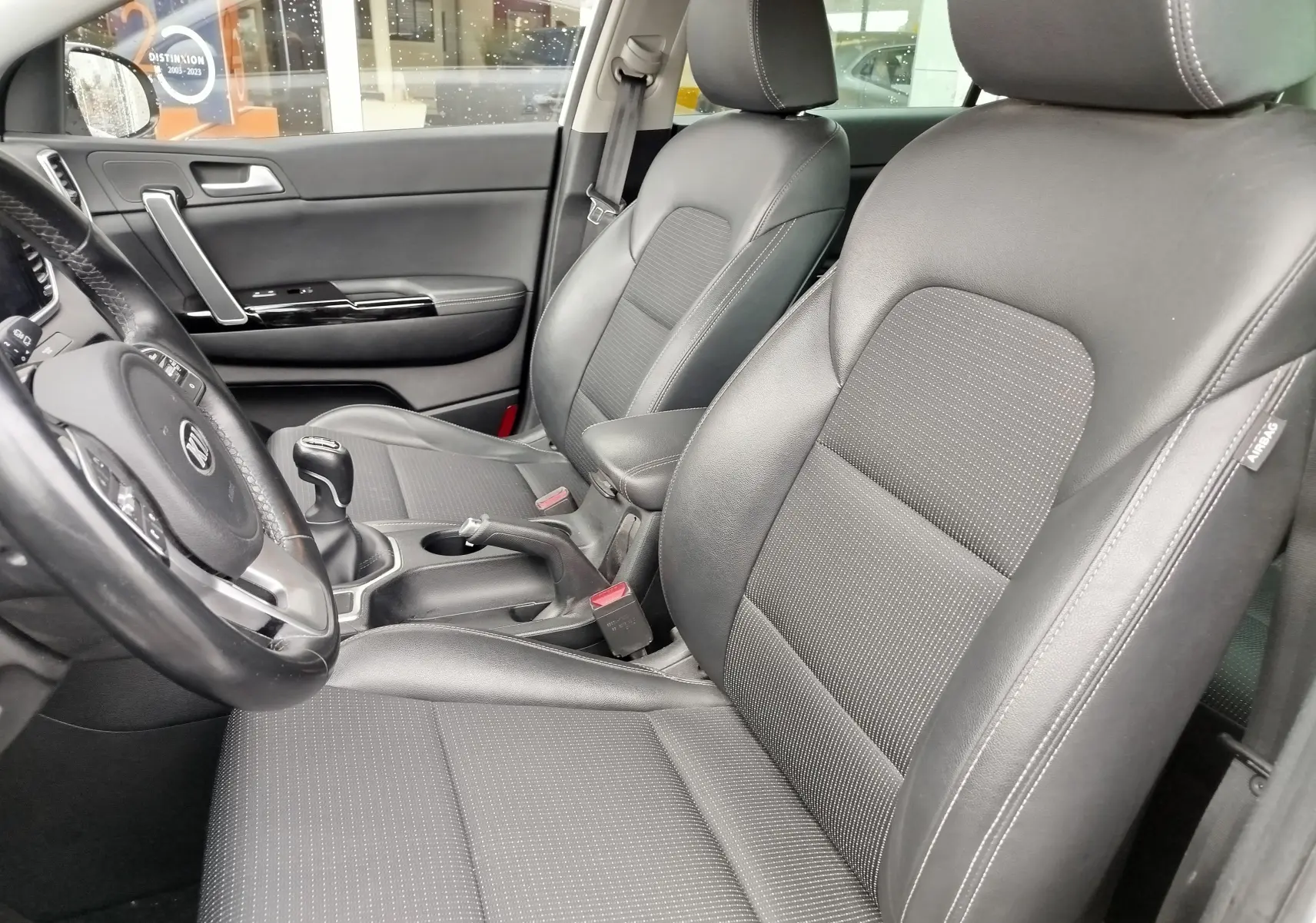 Vue intérieure côté conducteur du Kia Sportage 2022 blanc, sièges en cuir noir avec surpiqûres blanches et volant multifonction.