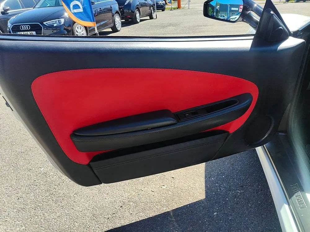 Intérieur de la porte côté gauche d'une Ferrari F430 Spider blanche, avec garniture rouge et noire visible.