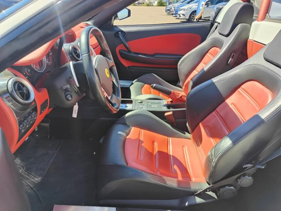 Intérieur de la Ferrari F430 Spider blanc, vue côté conducteur, sièges cuir noir et rouge avec tableau de bord assorti.