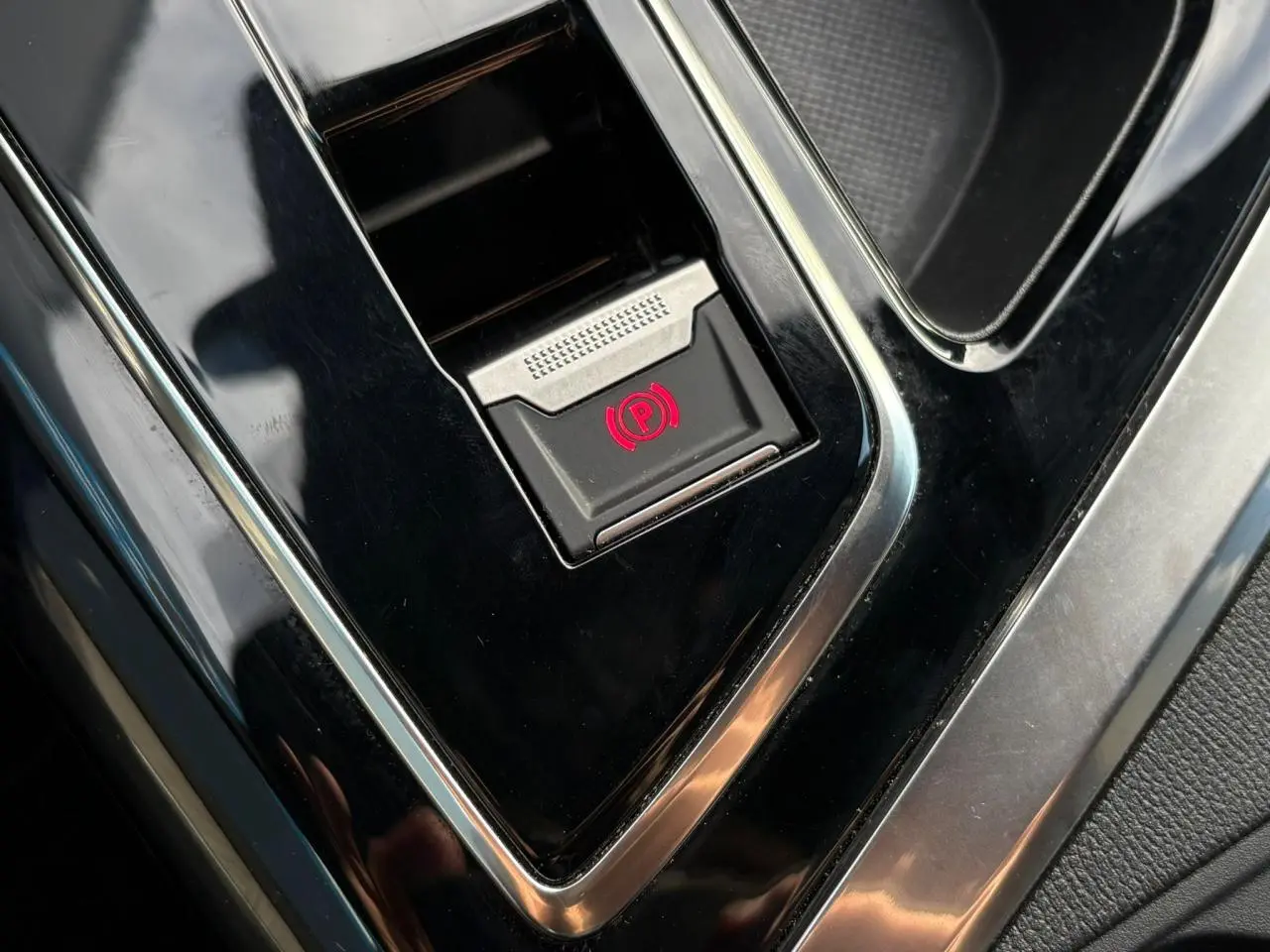Gros plan sur le bouton de frein de stationnement électrique dans la console centrale noire brillante du Peugeot 3008 2023.