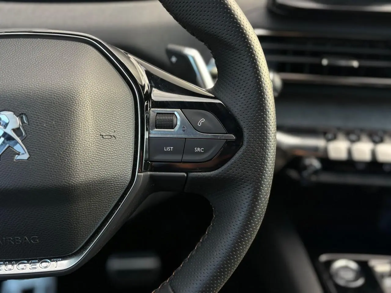 Gros plan sur le volant cuir perforé à droite du Peugeot 3008 2023, avec commandes intégrées et finition noire brillante.