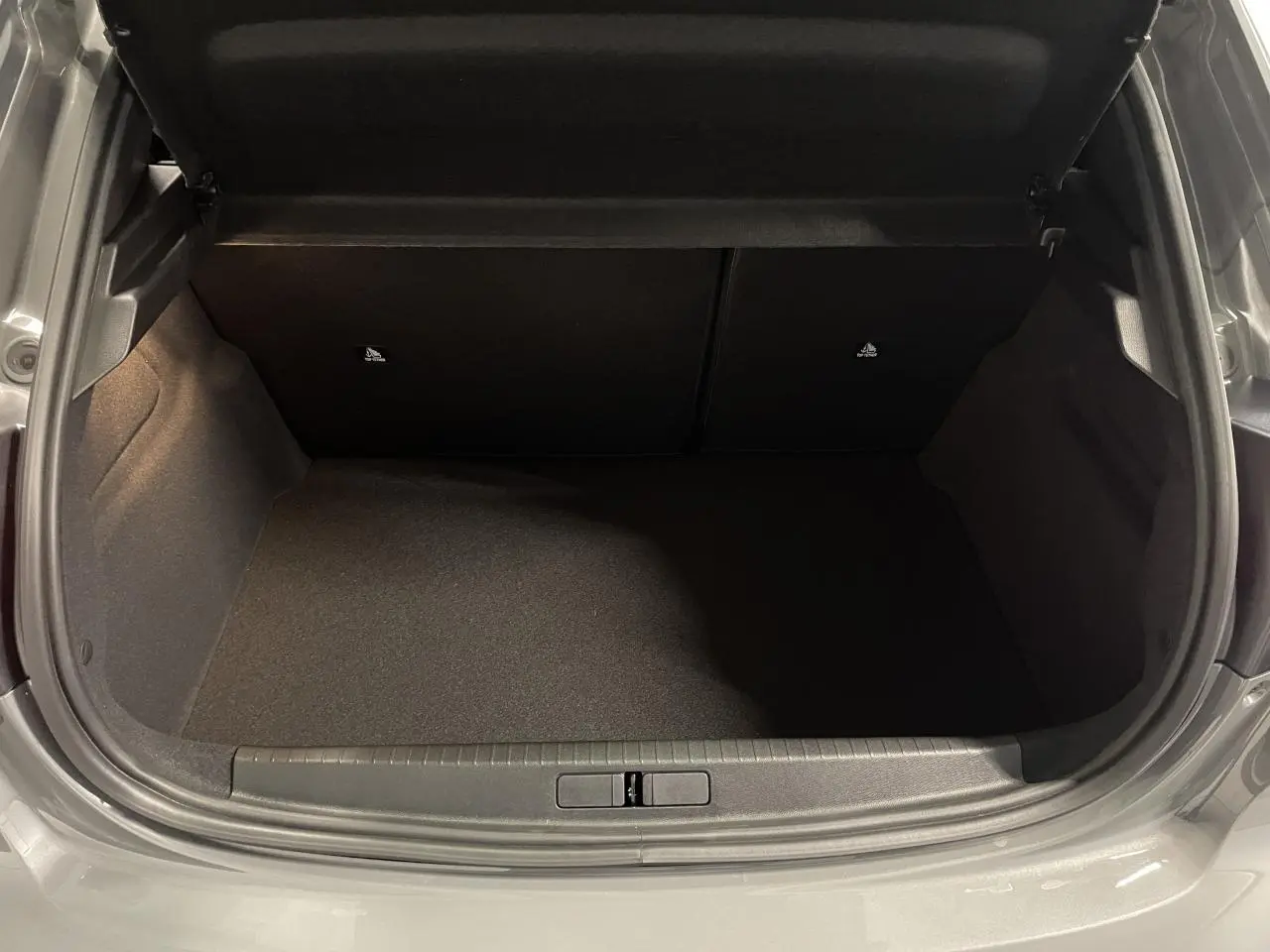 Coffre ouvert vu de l'arrière d'une Peugeot 208 gris selenium, montrant l'espace de chargement vide.