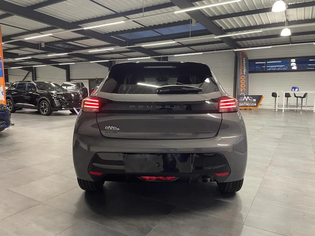 Vue arrière d’une Peugeot 208 hybride gris sélénium avec feux arrière LED allumés dans un showroom.