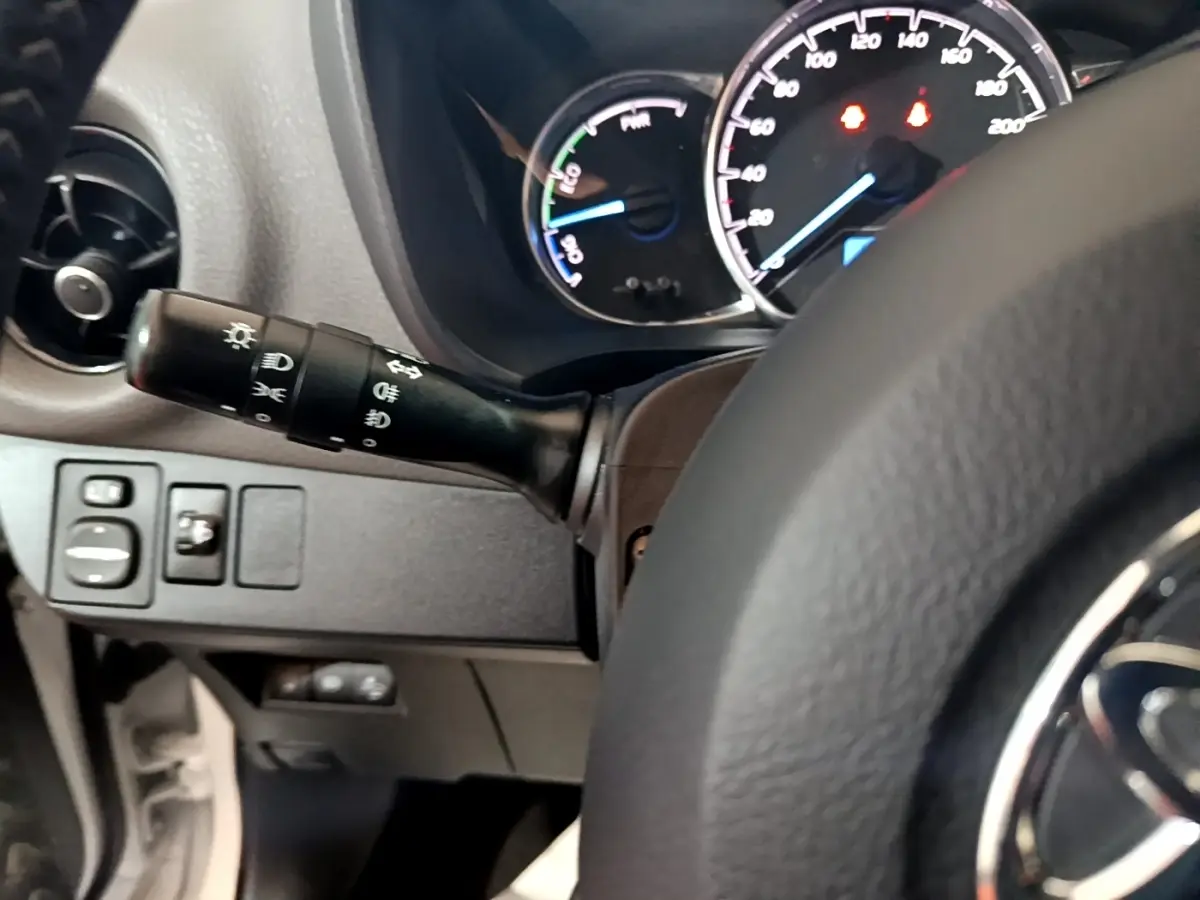 Vue rapprochée du tableau de bord et du commodo gauche de la Toyota Yaris hybride blanche, avec compteurs éclairés.