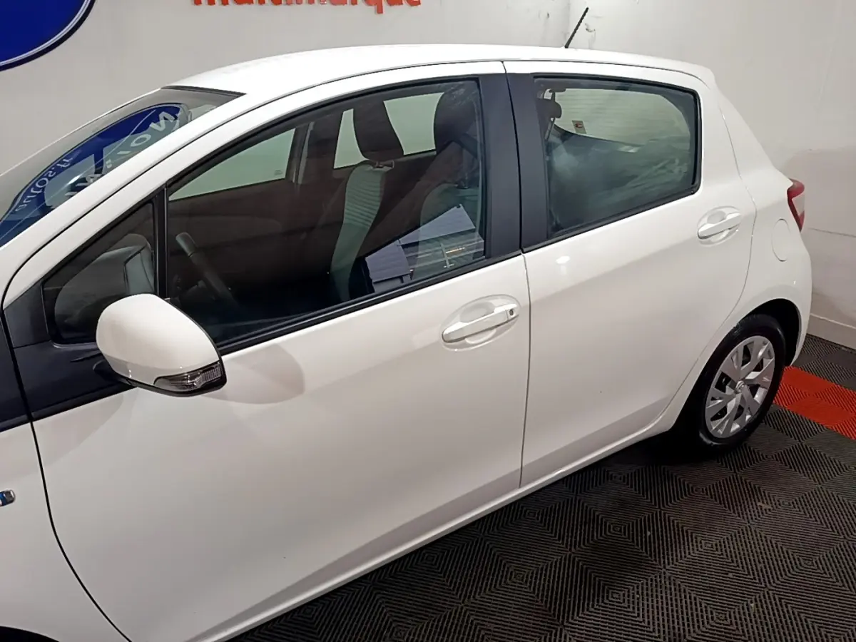 Vue de profil côté gauche d'une Toyota Yaris blanche 5 portes, avec rétroviseur blanc et jantes compactes.