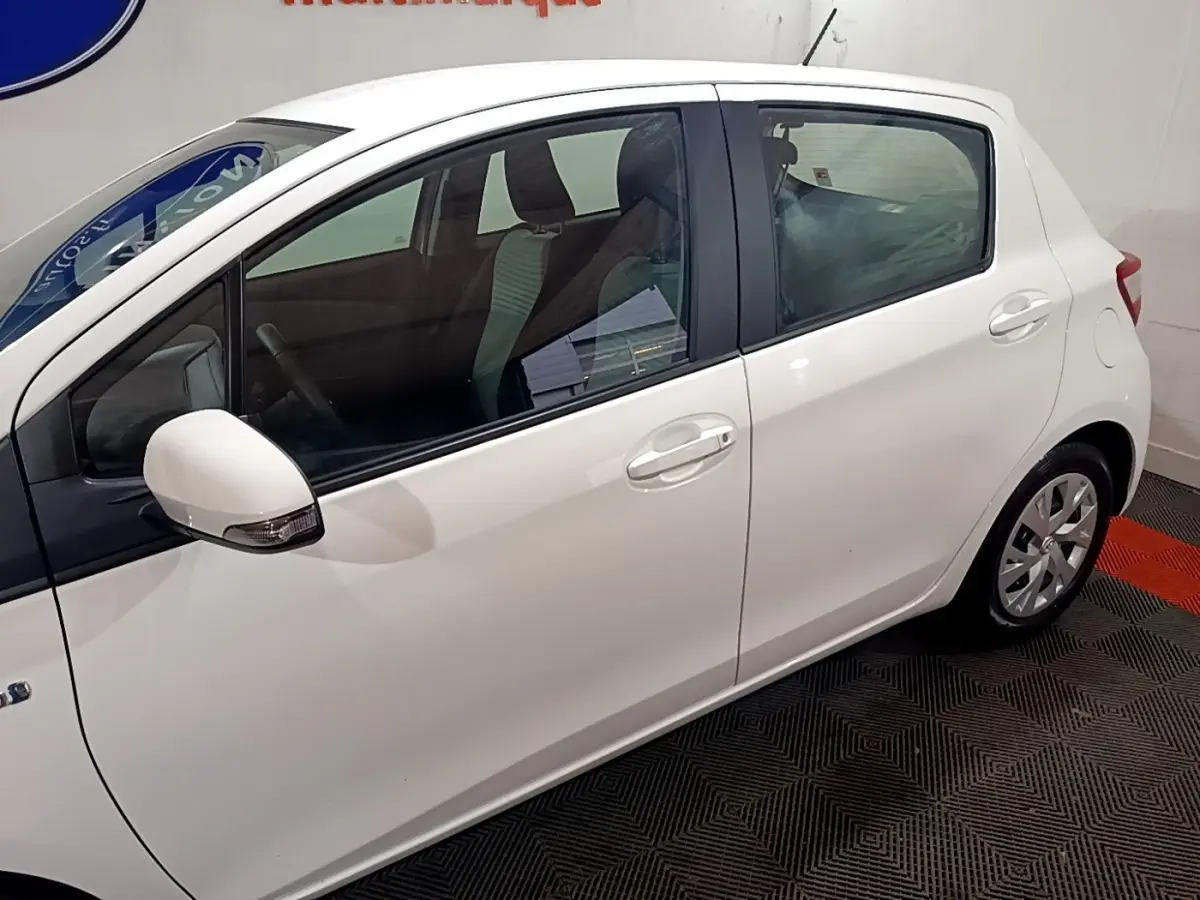 Vue de profil côté gauche d'une Toyota Yaris blanche 2019 hybride en intérieur, avec rétroviseur et poignées assortis.