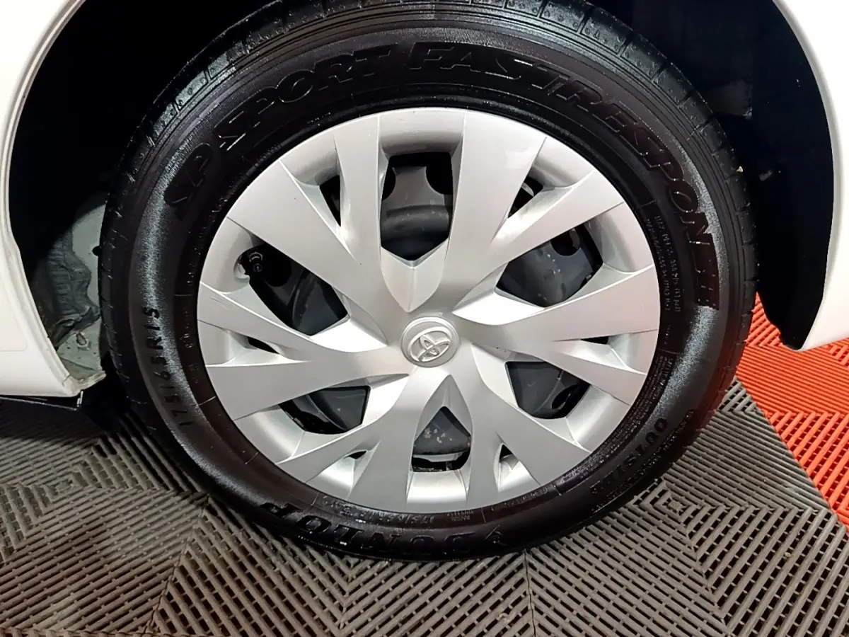 Gros plan sur la roue avant gauche d'une Toyota Yaris blanche, avec jante en alliage argentée et pneu noir.