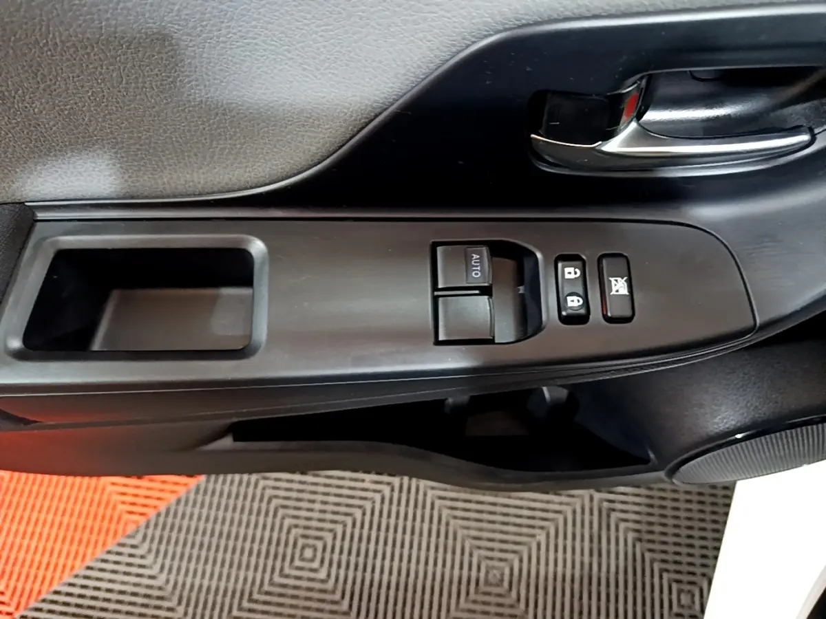 Gros plan sur la commande de lève-vitre et verrouillage sur la portière avant gauche d'une Toyota Yaris blanche.