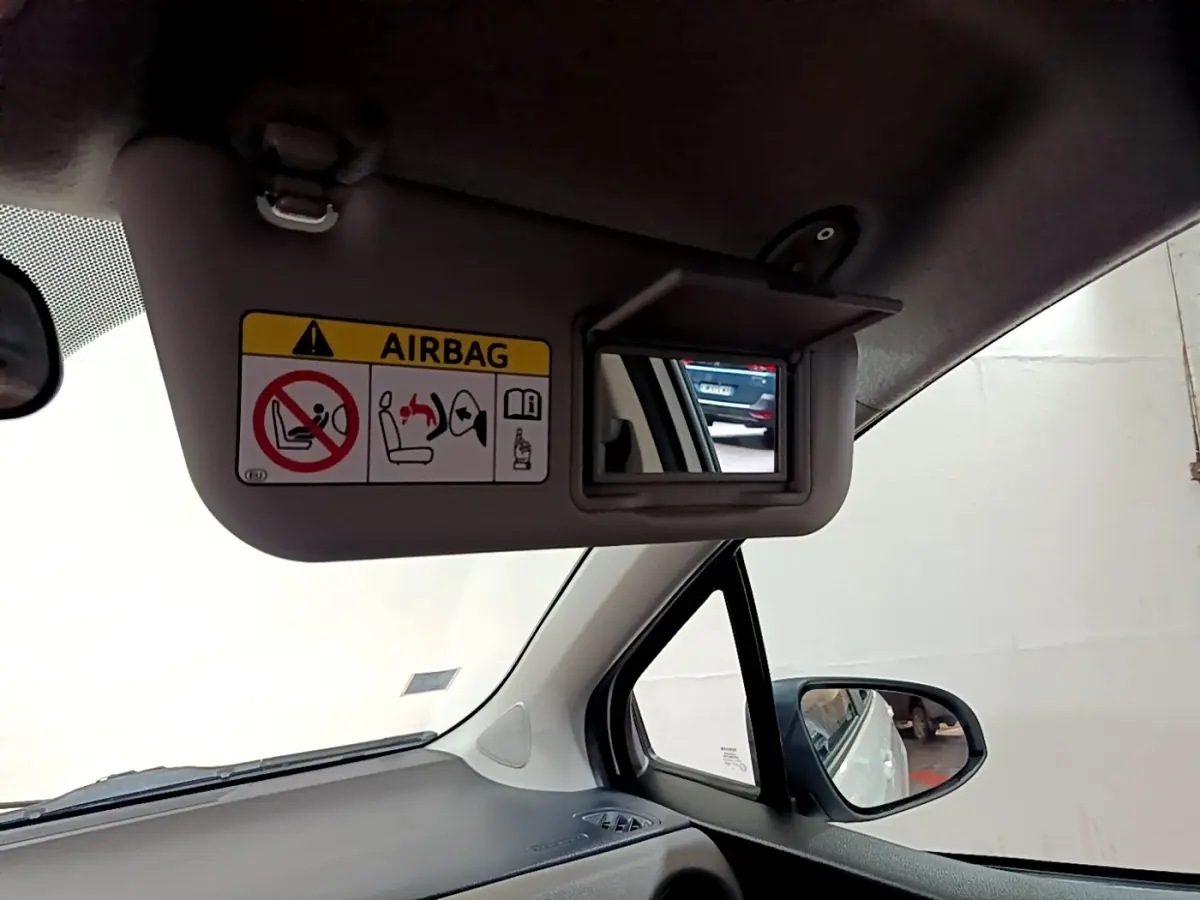 Vue intérieure côté conducteur sur le pare-soleil avec miroir et avertissement airbag de la Toyota Yaris blanche.